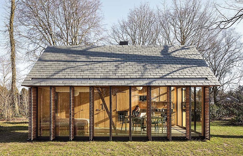 Windows with wood slat shutters line the side wall of this modern cottage, creating an open feeling, while at night, the shutters can be closed for more privacy.