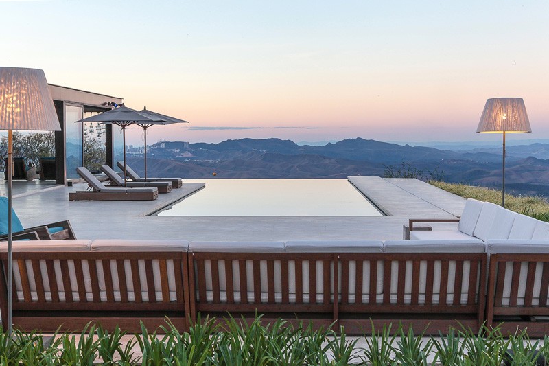 An infinity edge swimming pool with a deck that's furnished with sun loungers and a couch.