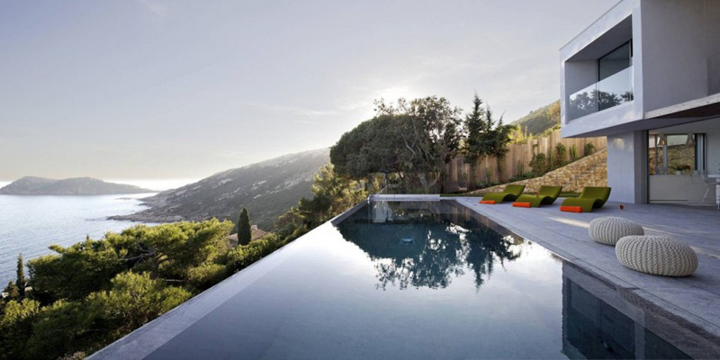An infinity edge swimming pool with a concrete deck overlooks the waters of Saint Tropez.