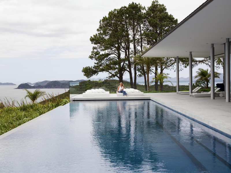 An infinity edge swimming pool with a concrete deck overlooks the New Zealand landscape.