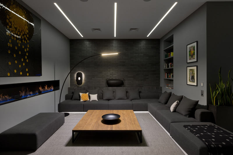 A dark living room with built-in shelving, a linear fireplace, and a couch that wraps around the corner. #LivingRoomIdeas #ModernLivingRoom