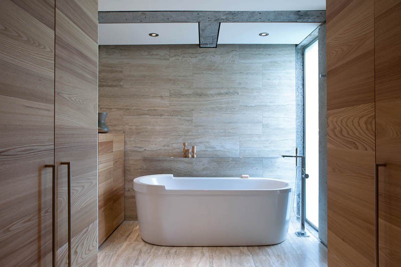 A standalone bathtub sits in a contemporary bathroom next to a limestone wall