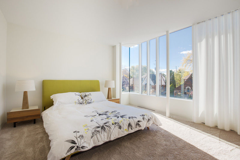 This bedroom has a wall of windows with a sheer white curtain.