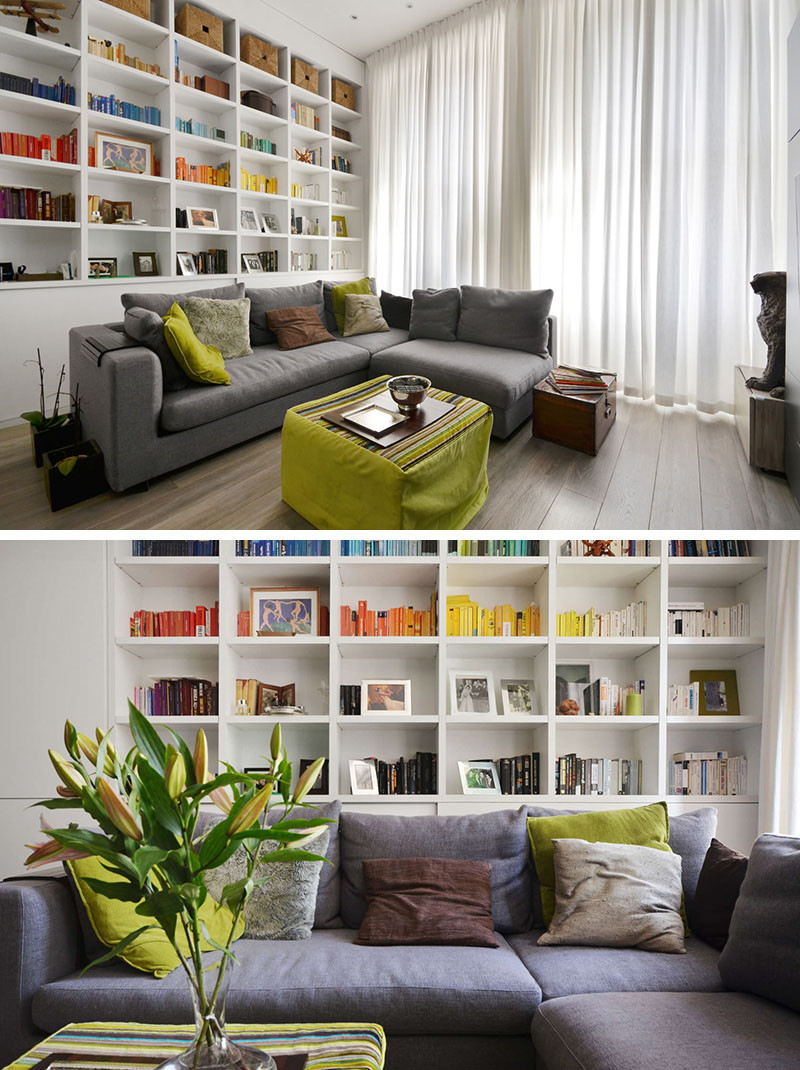 This apartment, designed by Daniele Petteno Architecture Workshop, has a mostly monochrome palette with pops of color added to the decor, with with a green coffee table and pillows, as well as books have been color-organized.