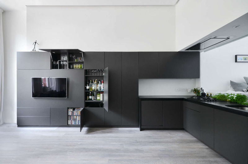 The black kitchen cabinets wrap around the wall and become the entertainment center in this apartment in London.