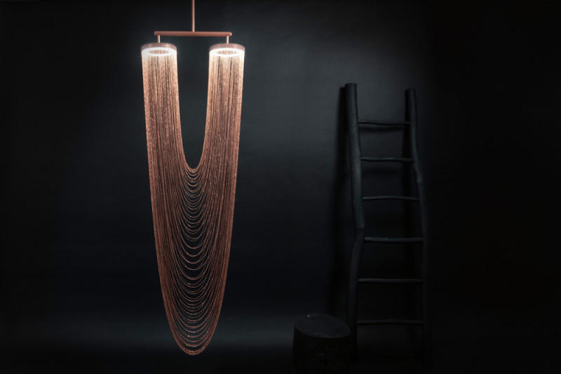 These sculptural lights are made from delicate copper plated chains that hang from two circular forms to create a unique curved shape, all of which is illuminated by a ring of LED lights. #Lighting #SculpturalLighting #LightingDesign #Chandelier #CopperLighting