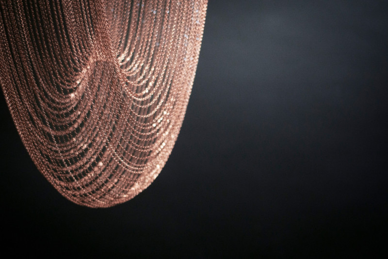 These sculptural lights are made from delicate copper plated chains that hang from two circular forms to create a unique curved shape, all of which is illuminated by a ring of LED lights. #Lighting #SculpturalLighting #LightingDesign #Chandelier #CopperLighting