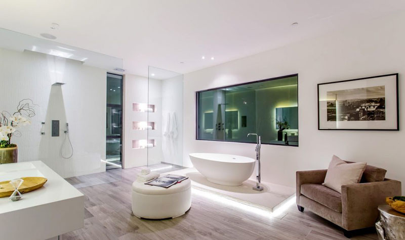 This master bathroom has a floor to ceiling glass partition for the shower, and the bathtub has been raised on a platform surrounded by hidden lighten.