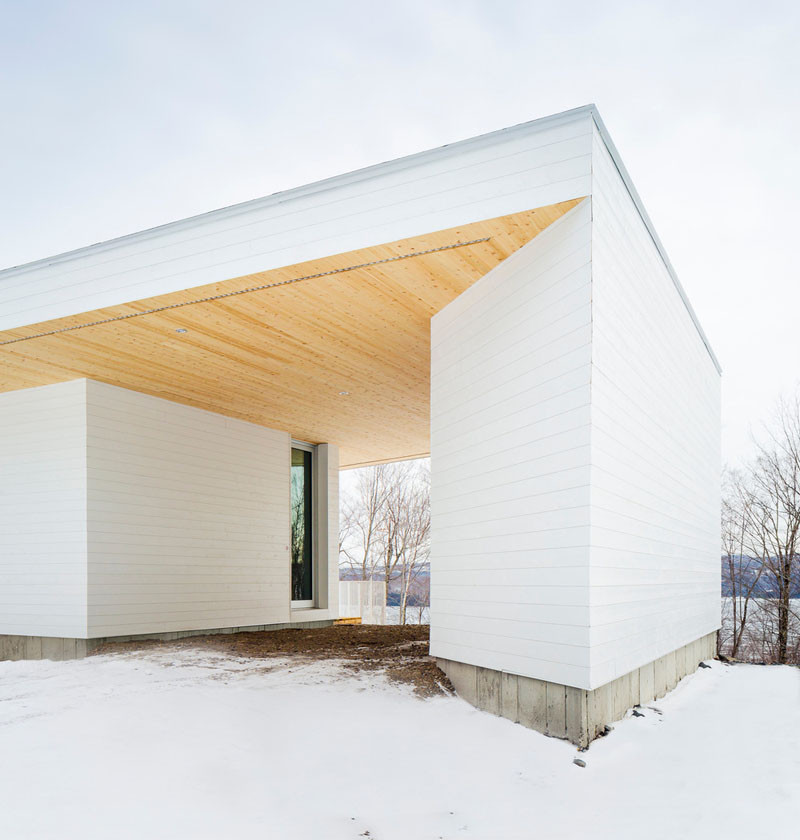 The white painted wood siding of this home in Quebec, is broken up by the light cedar wood on the roof soffits.