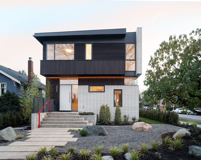 This contemporary home, with a facade of white brick, is located on a corner lot in a quiet neighborhood of Vancouver, Canada. The home, designed by architect Randy Bens, also has dark stained cedar siding running vertically and horizontally, and zinc colored metal trim.
