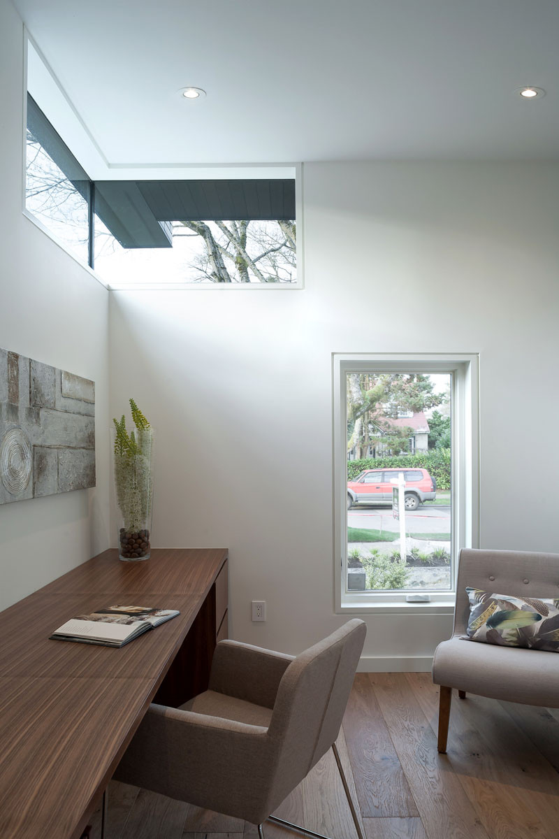 This home office, with wooden walnut desk, has views of the street through a small vertical window.