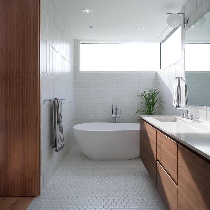 This bathroom features a walnut vanity with a white countertop. Two different styles of white tiles have been included in the design.