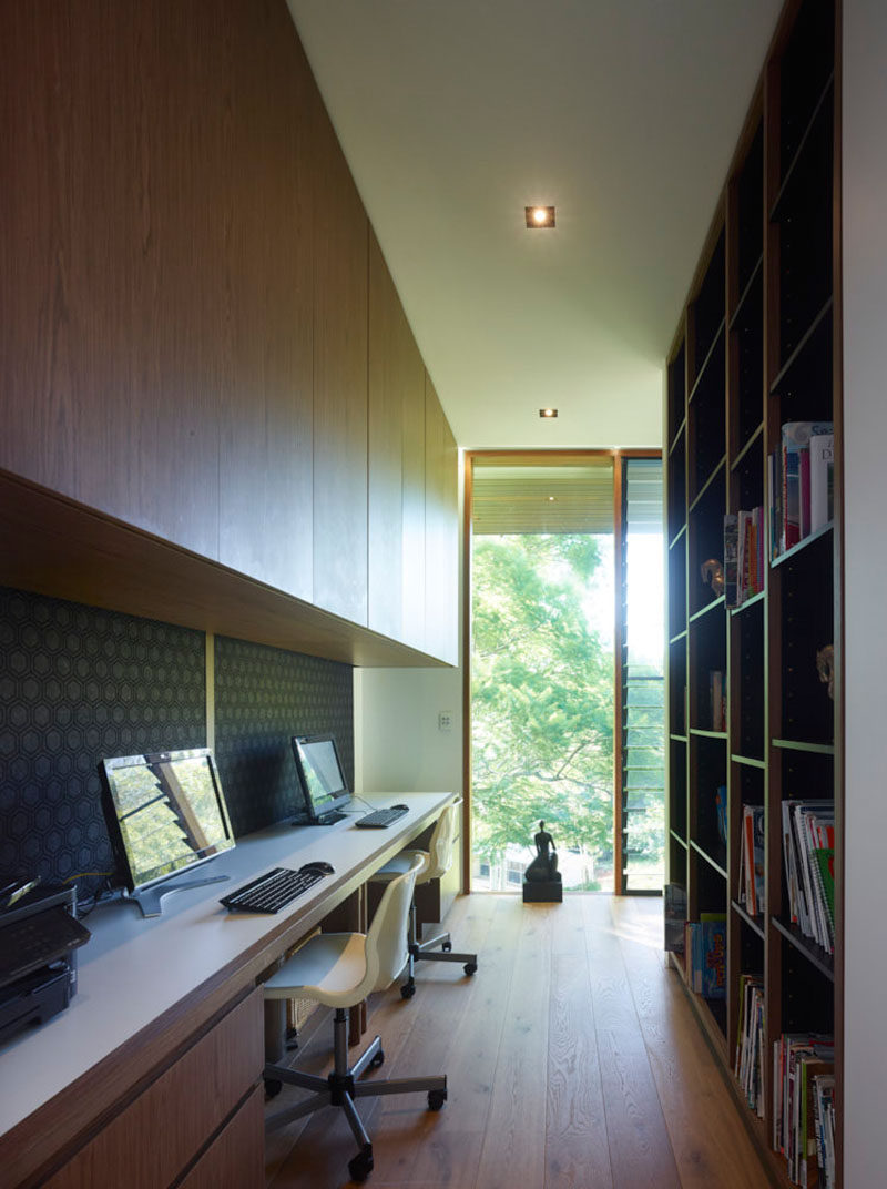 This home office has a built-in desk with cabinetry and a bookshelf. A window at the end of the room lets lots of natural light in.