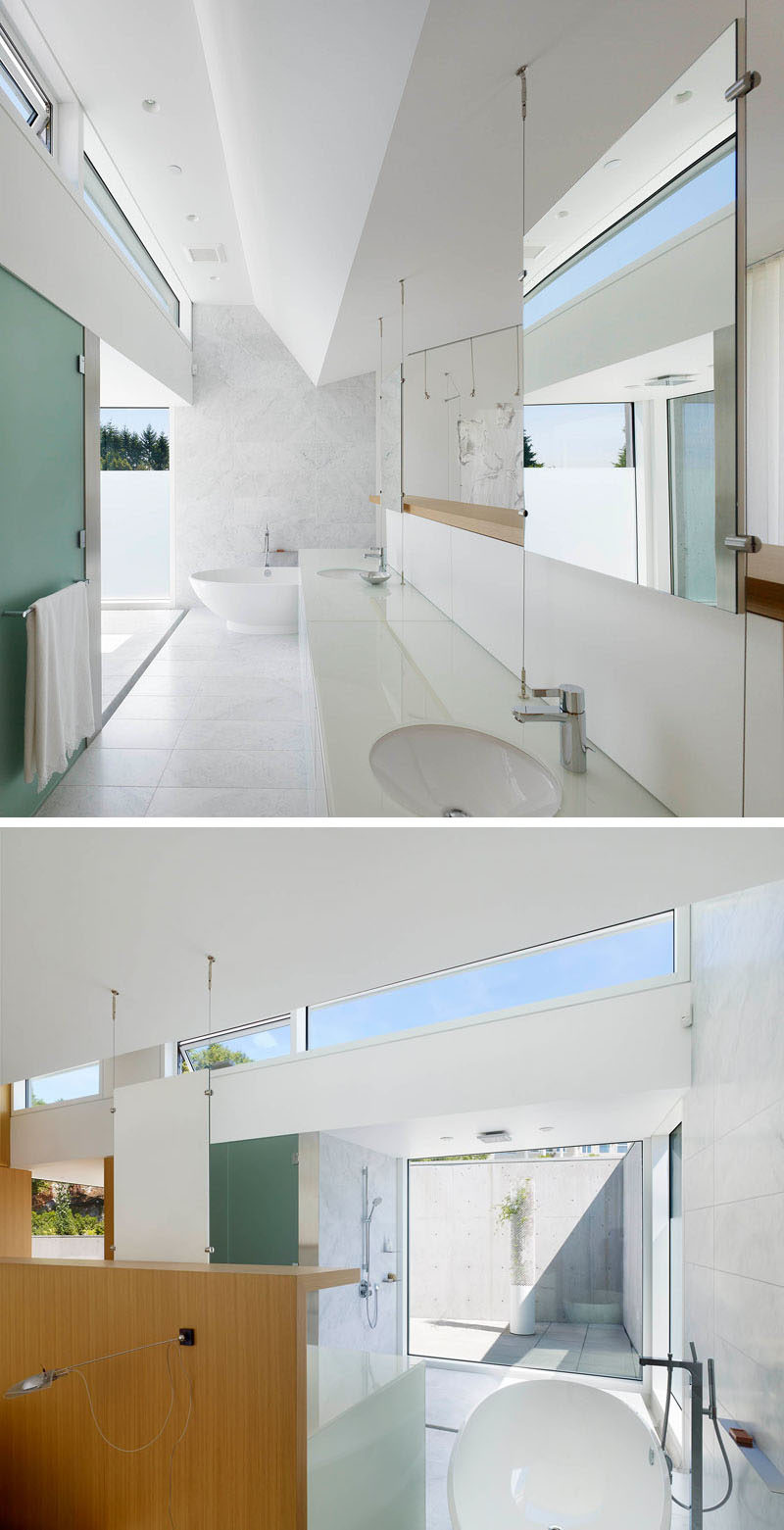 This bright white bathroom has hanging mirrors, touches of wood, and lots of natural light from the floor to ceiling window in the shower.