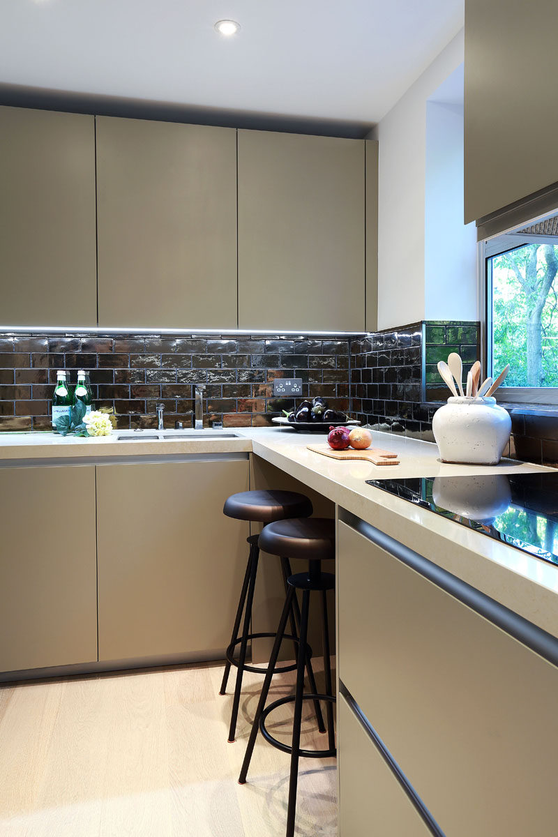 Pale khaki cabinetry, cream colored countertops, and dramatic dark bronze tiles make up the color palette in this kitchen.