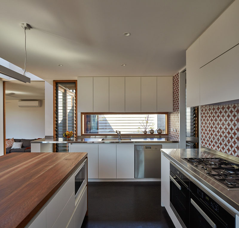 This kitchen has been designed with white cabinets, wood and stainless steel countertops and a red and white patterned backsplash..