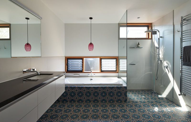 This bathroom has a glass enclosed shower, and tiles that seamlessly flow from the shower to the bathtub surround.