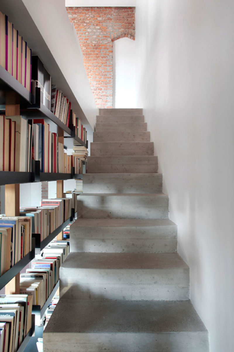 9 Stylish Staircases With Bookshelves As Safety Rails // These concrete stairs are brightened up by the light shining through the open bookshelf.