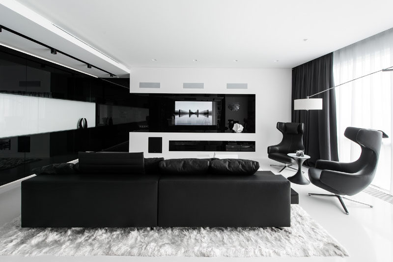 In the living room of this black and white themed apartment, the television is built-in behind the black glass, and when the TV is off, the whole wall looks like a black and white architectural detail.