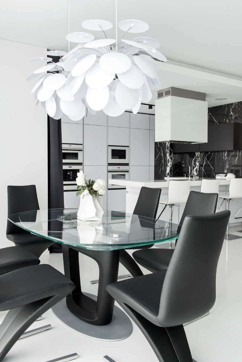 In this black and white home, the dining area has sculptural white pendant lights hanging above a glass top dining table and elegant black chairs.