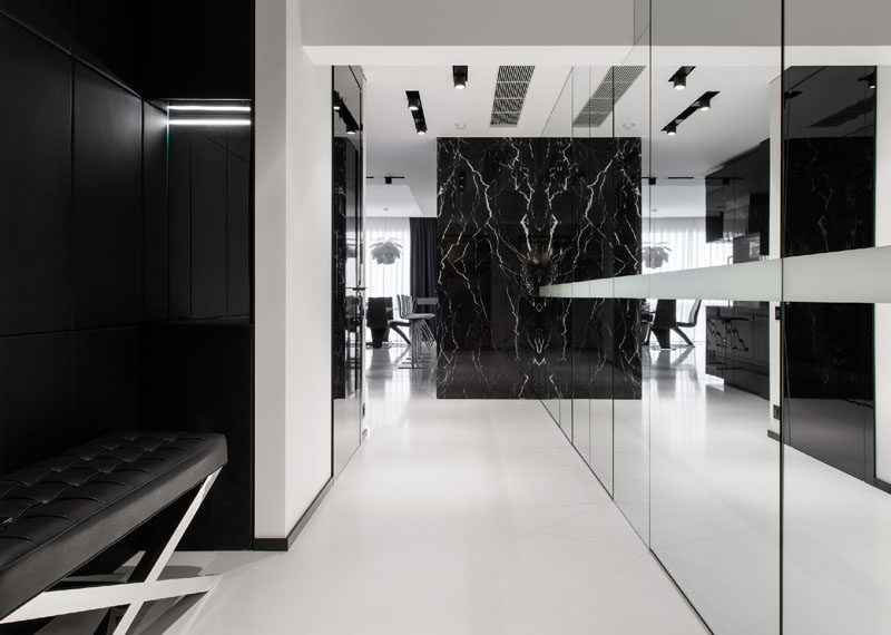 This black and white hallway has a wall of mirrored glass to reflect the light, make the space appear larger and hide additional storage.