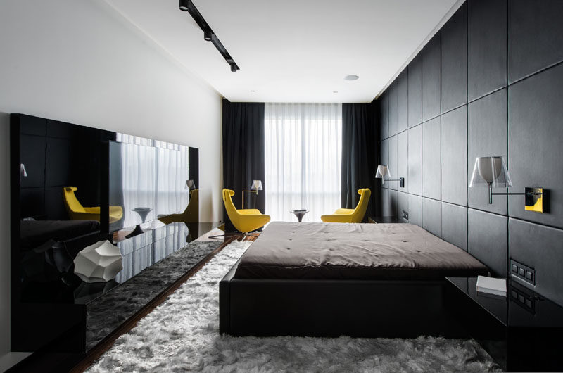 In this black and white bedroom, one wall is entirely covered in custom-designed black leather panels that act as a headboard as well as a decorative feature for the room. A pop of color has been introduced with bright yellow chairs, that have been used draw your eye to the window.