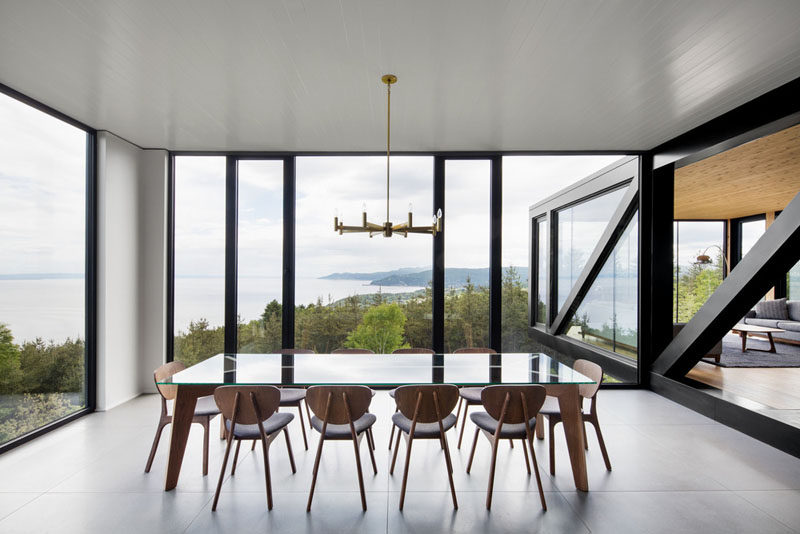 This dining room with amazing views, has floor-to-ceiling windows, a glass and wood dining set that seats 10, and a gold chandelier.