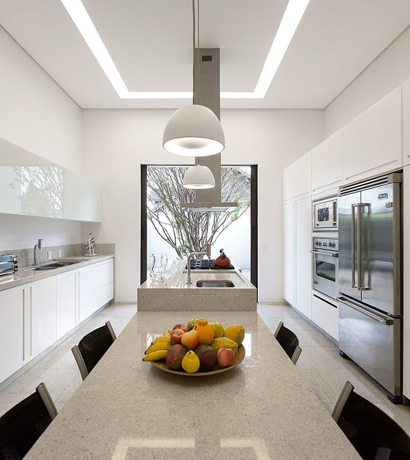 This kitchen, with its white cabinetry, has a large picture window at the end that perfectly frames the tree outside, and also lines up with the kitchen island.