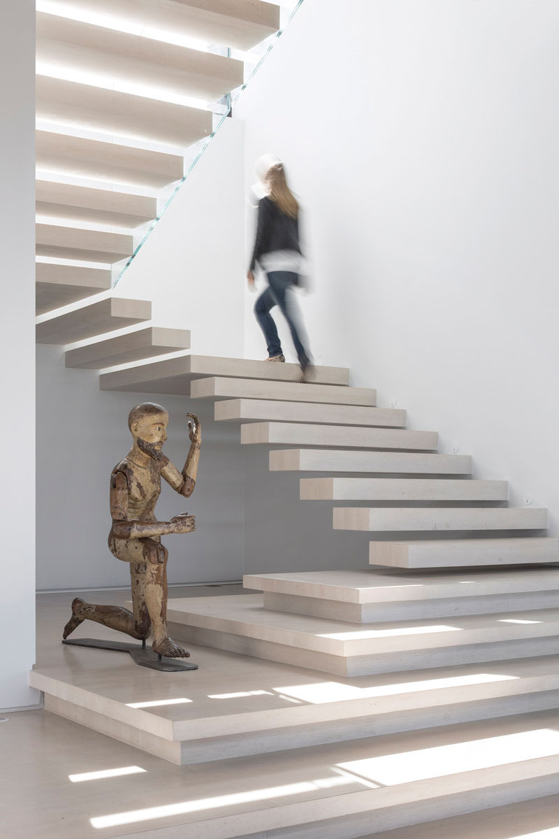 Light colored stone floating stairs with a space for a sculpture, lead you upstairs in this home.