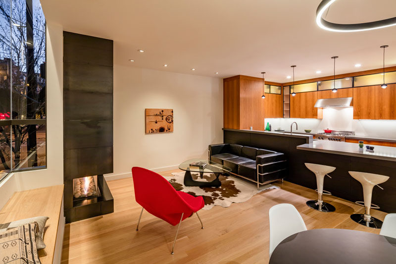 This open plan living, dining and kitchen area, has a fireplace and tv tucked into the corner, and a U-shaped wooden kitchen with gray countertops.