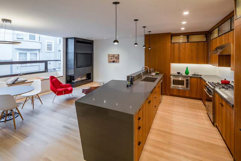 This open plan living, dining and kitchen area, has a fireplace and tv tucked into the corner, and a U-shaped wooden kitchen with gray countertops.