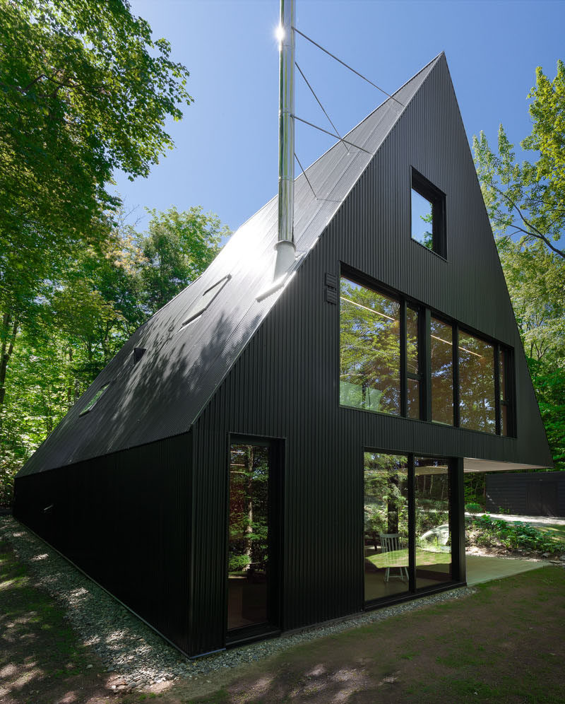 This black cottage with a sloping roof line, is surrounded by a Hemlock forest in Quebec, Canada.