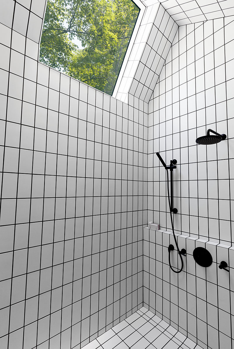 This bathroom has white tiles, but they have used black grout to match the shower heads and taps. There's also a skylight to provide extra light to the bathroom.