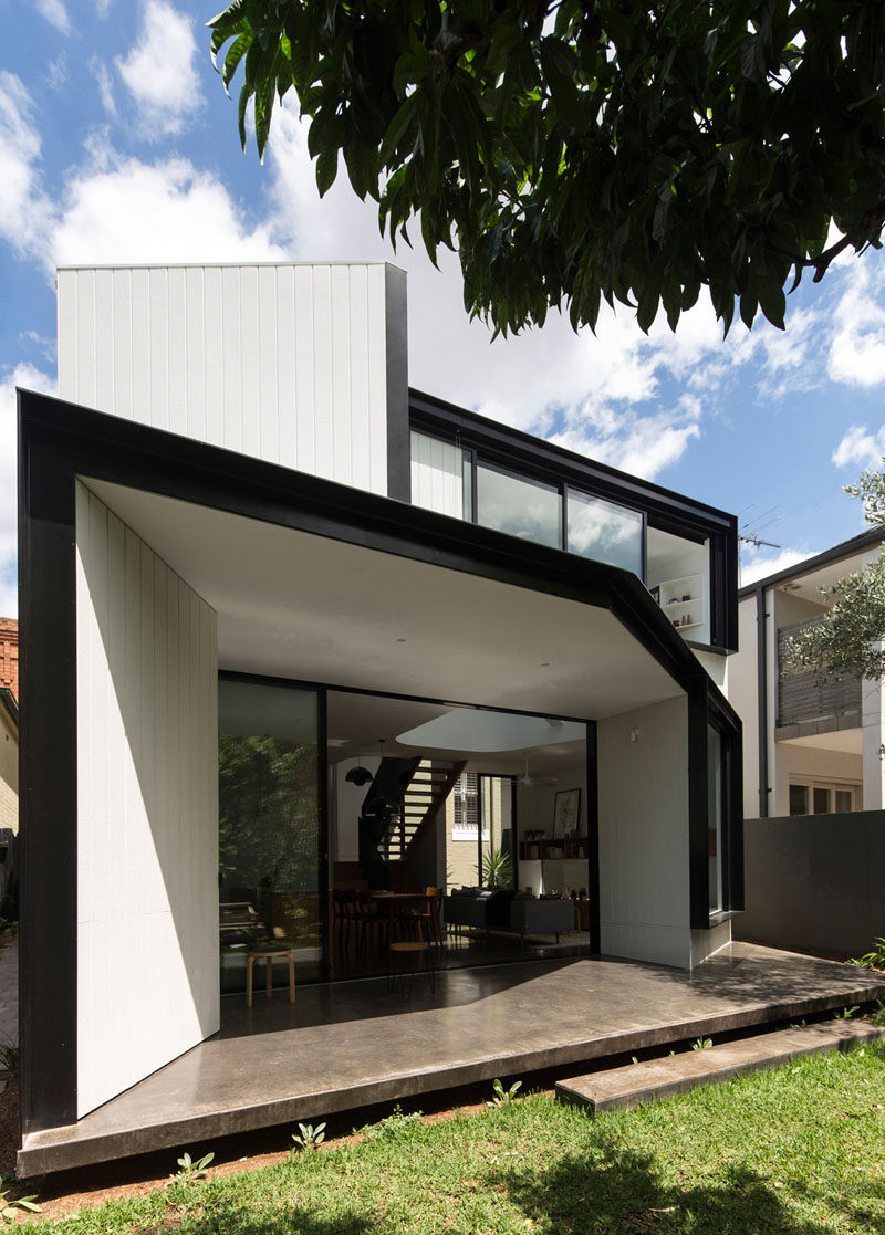 Black frames and concrete patio contrast the white siding and interior of this house extension in Sydney, Australia.