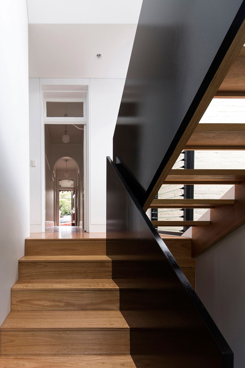 Wood stairs with a black safety railing and white walls.