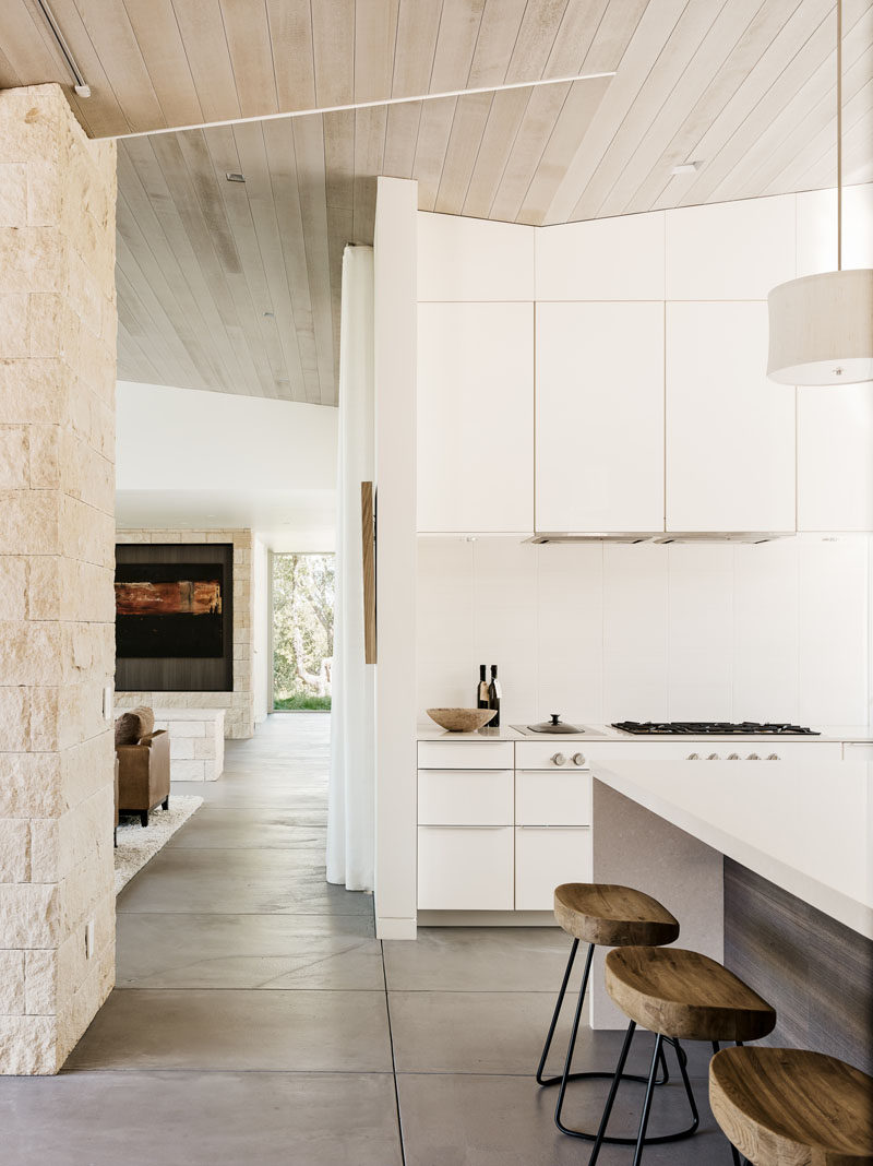 This kitchen is full of white cabinetry, has a large kitchen island with seating, windows that face a courtyard and cedar-clad ceilings.