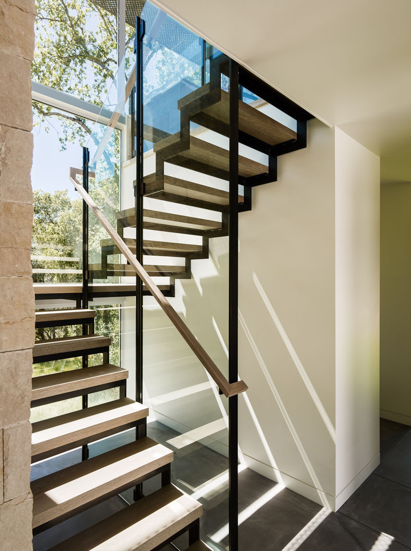 Wood and steel stairs lead you to the upper floor of this home, with large windows flooding the area with sunlight.