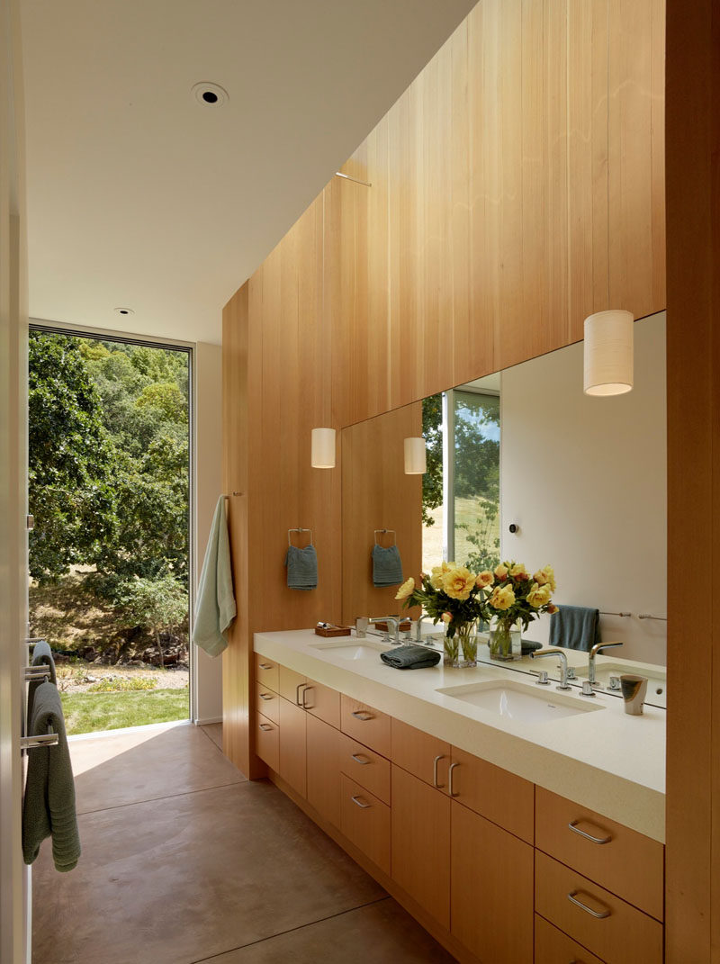 This mostly wooden bathroom with dual vanities, is filled with natural light from a sky light and floor-to-ceiling windows.