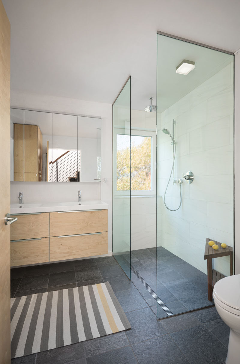 This contemporary bathroom has a glass shower stall with a rain shower head, and a window for looking at the trees while showering.