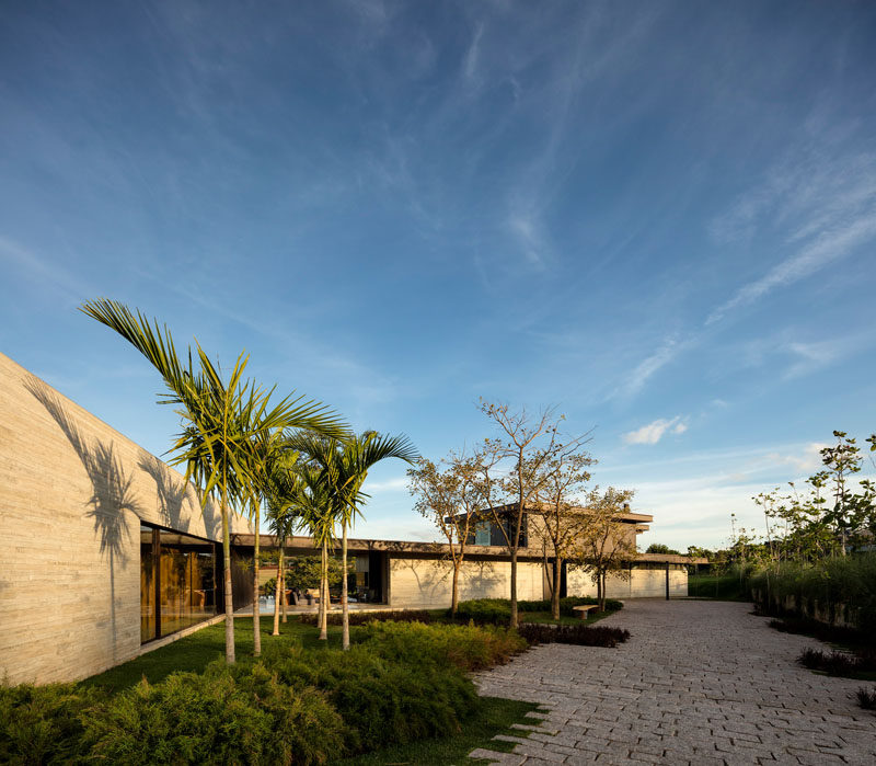 The entrance to this home features a stone driveway and a landscaped yard with a spot for a bench.