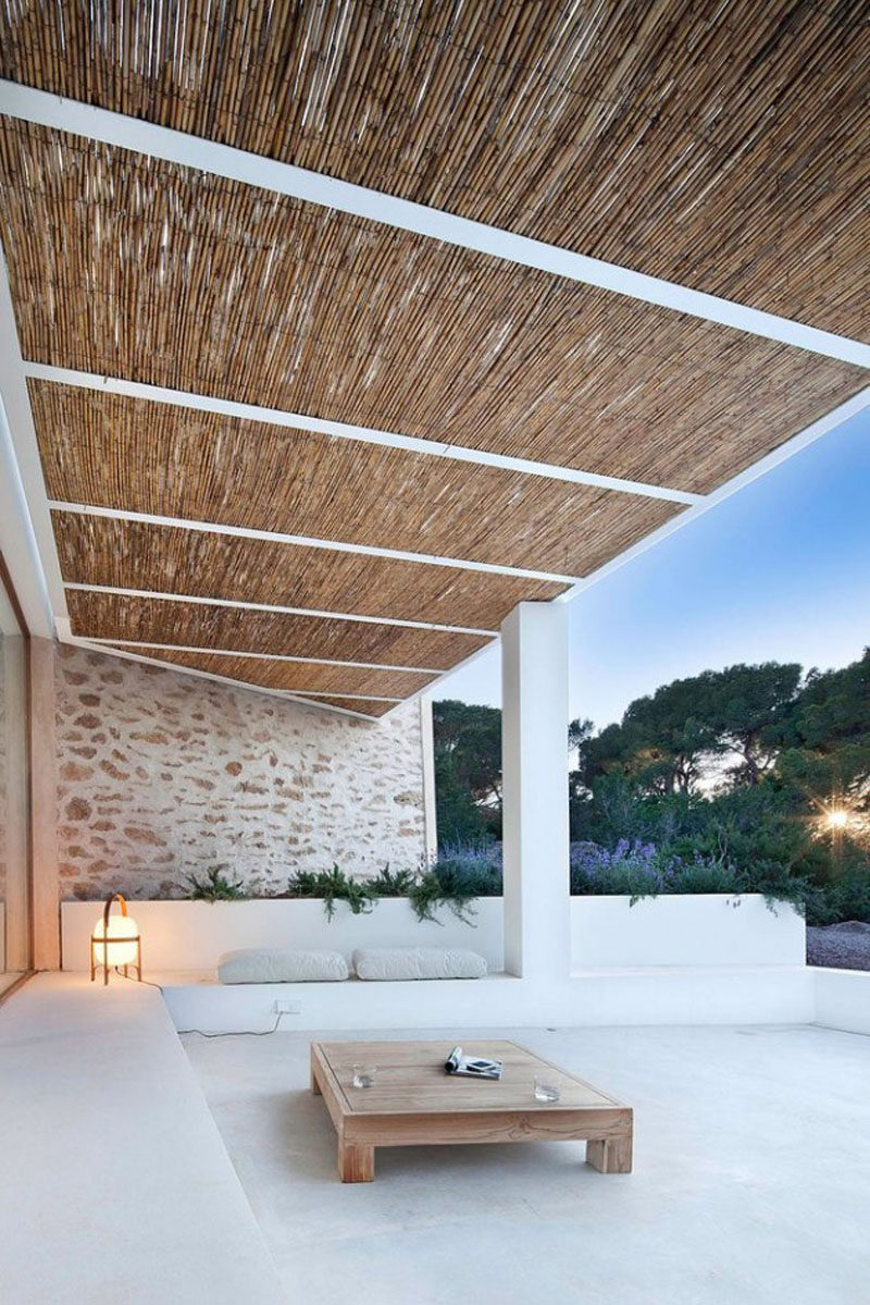 This relaxing, covered outdoor space has built-in seating, a light stone wall, and a bamboo roof.