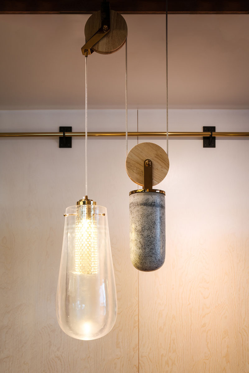 The custom-designed pendant lights that are on a pulley system, consist of a drop pendant light made from cast resin, a counterweight made from cast concrete, and brass details with a diffused COB LED light within.