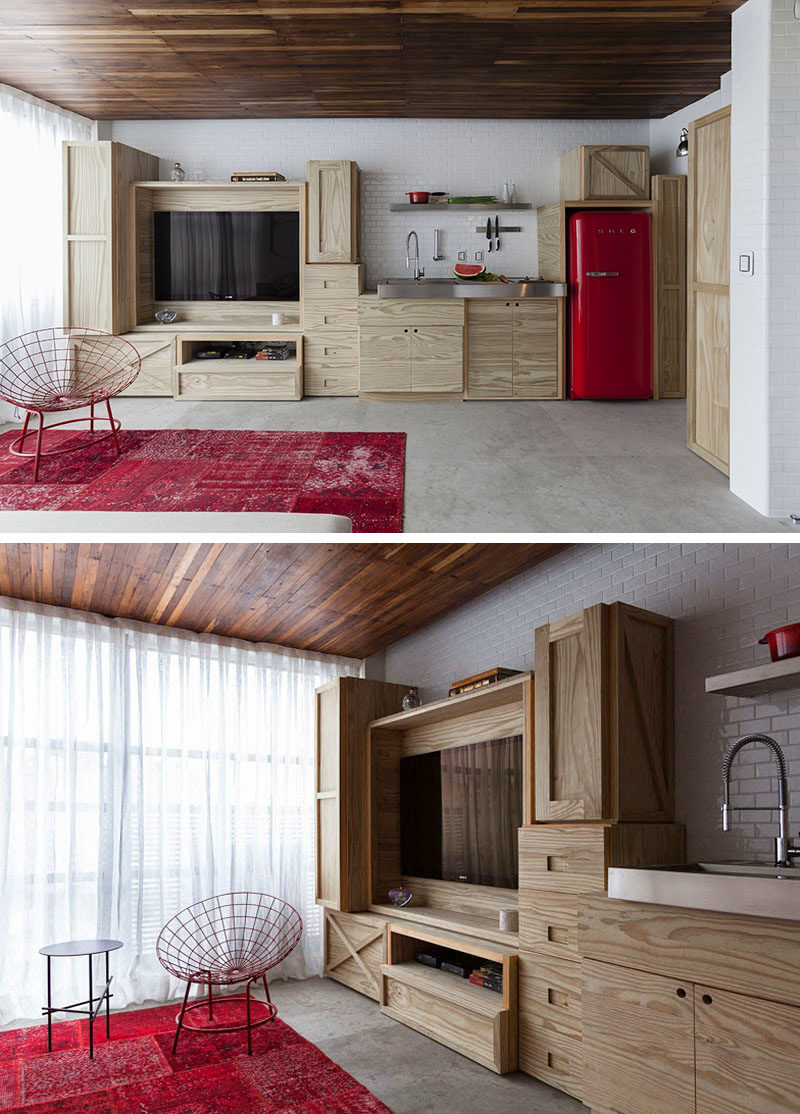 Along one wall in this small apartment is custom built cabinetry that combines the entertainment unit and the kitchen.