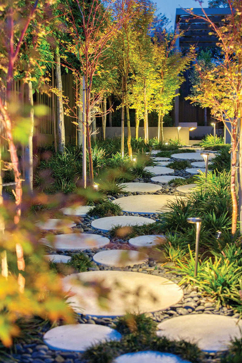 10 Ideas for Stepping Stones in Your Garden // Circular stepping stones surrounded by small pebbles, lights, and greenery create a pathway through this backyard.