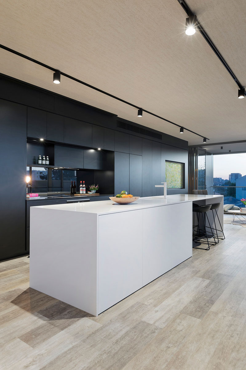 This kitchen has a long white island that directly contrasts the wall of black cabinetry.