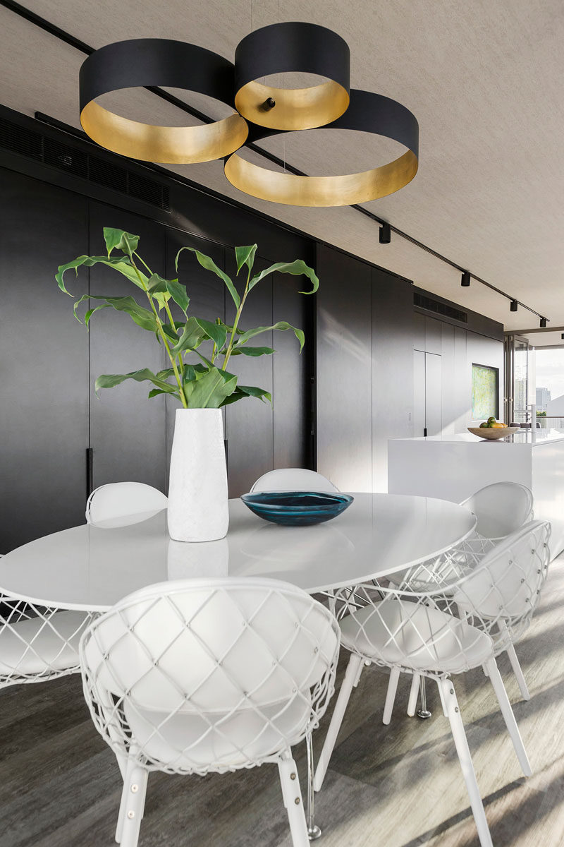 Black pendant lights above a round white dining table, perfectly match the black wall of cabinetry and the white island in the kitchen.