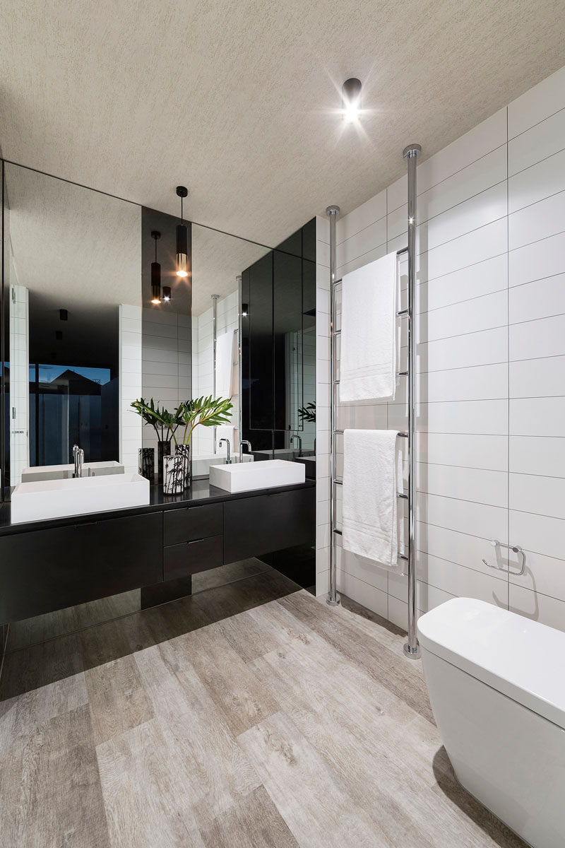 This bathroom has dual sinks, large white tiles, and a towel rack that goes from the floor to the ceiling.