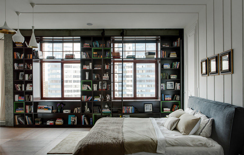 A bedroom has bookshelves that wrap around the wall, and art created from the electrical cords.