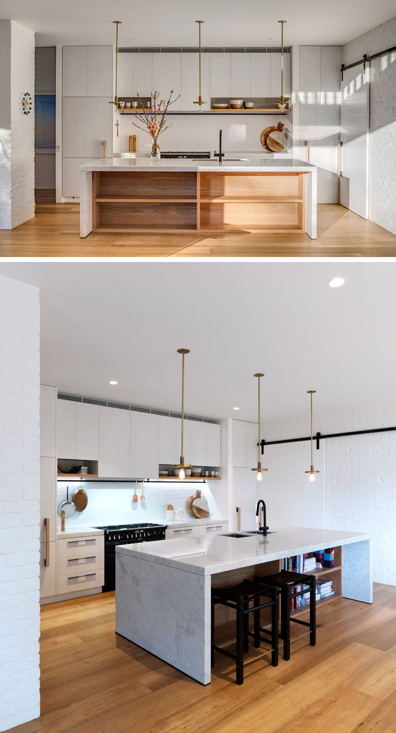 In this mostly white kitchen, the island has exposed storage and an overhang makes it possible for people to sit at while helping with food prep.