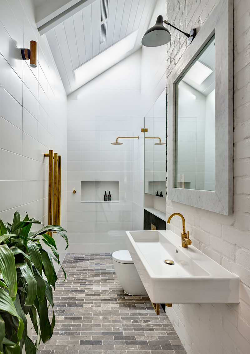 In this bathroom, white walls and ceilings make the brass accents and black cabinetry stand out. A skylight provides plenty of natural light to the space too.